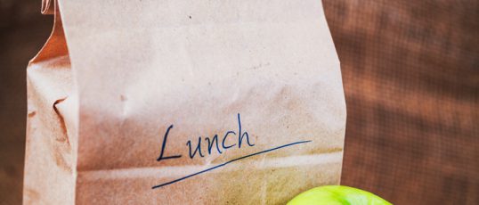 Brown bag lunch and green apple on canvas background and copy space